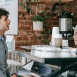 Two people chatting and smiling at a café counter, illustrating connection and community through everyday social interaction.